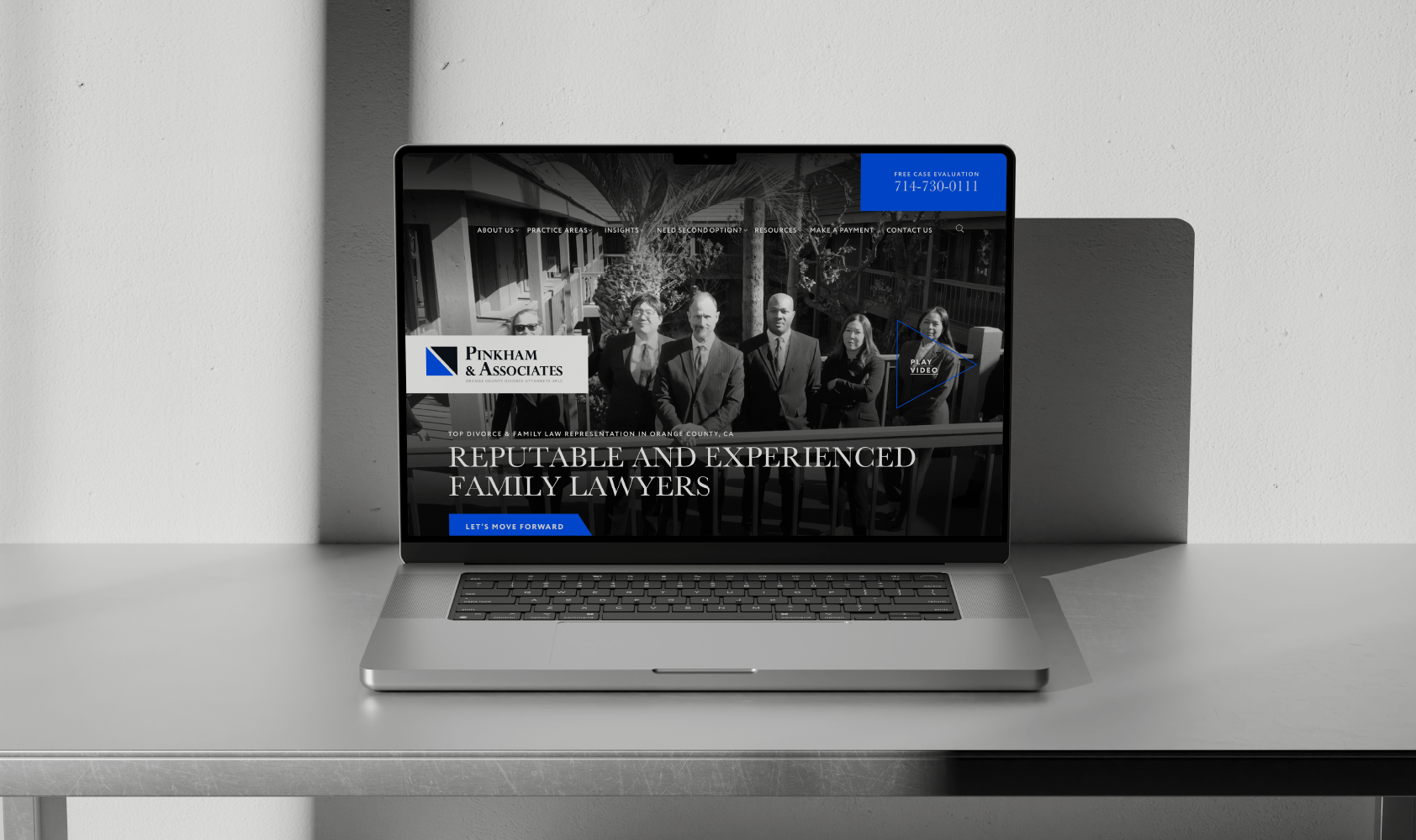 A laptop on a gray desk displays the Pinkham & Associates law firms website, featuring a black-and-white photo of four people and text reading Reputable and Experienced Family Lawyers.