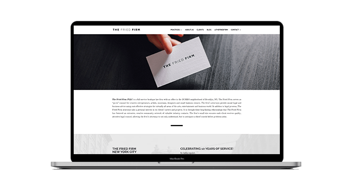 A laptop screen displays a website for The Fried Firm, showing a hand holding a business card with the firm’s name, a brief company description, and navigation links at the top.