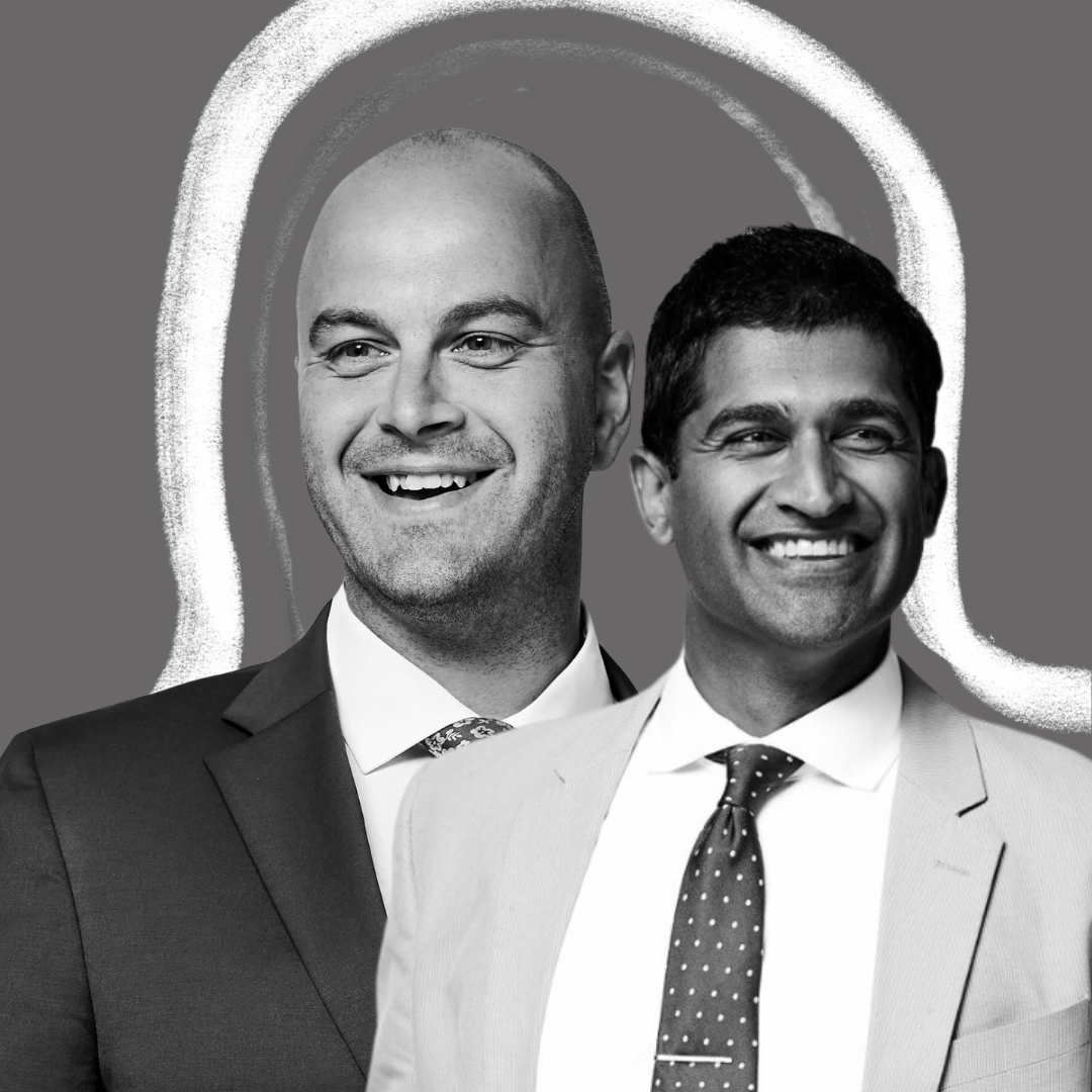 Two men wearing suits and ties smile while standing side by side against a gray background with a white chalk outline of a head behind them.