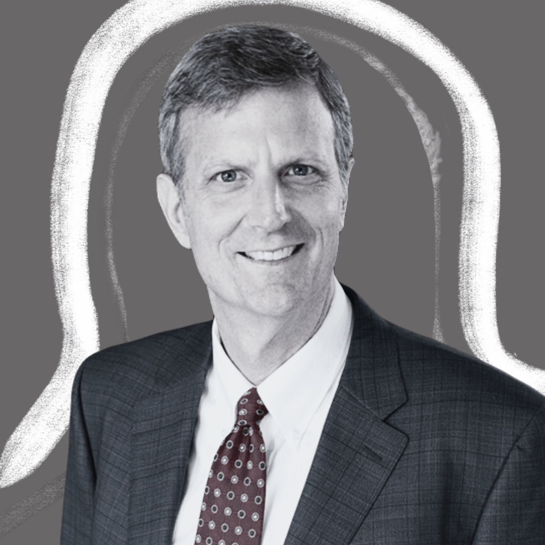 A man in a suit and patterned tie smiles at the camera. The background is gray with a white, abstract outline around his head and shoulders.